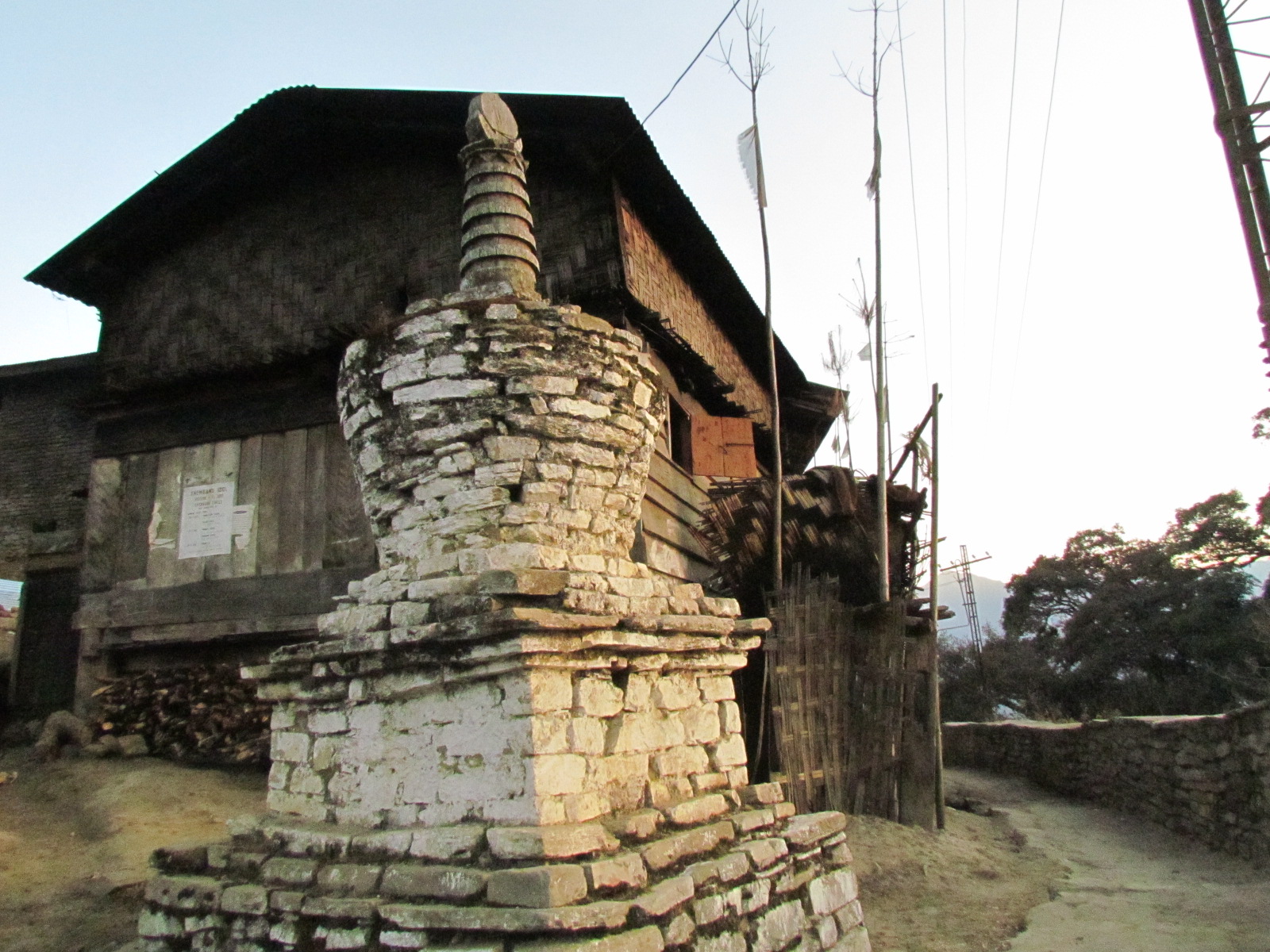 Whitewashed stone chorten beside a traditional timber and bamboo Monpa house at dusk in Thembang village