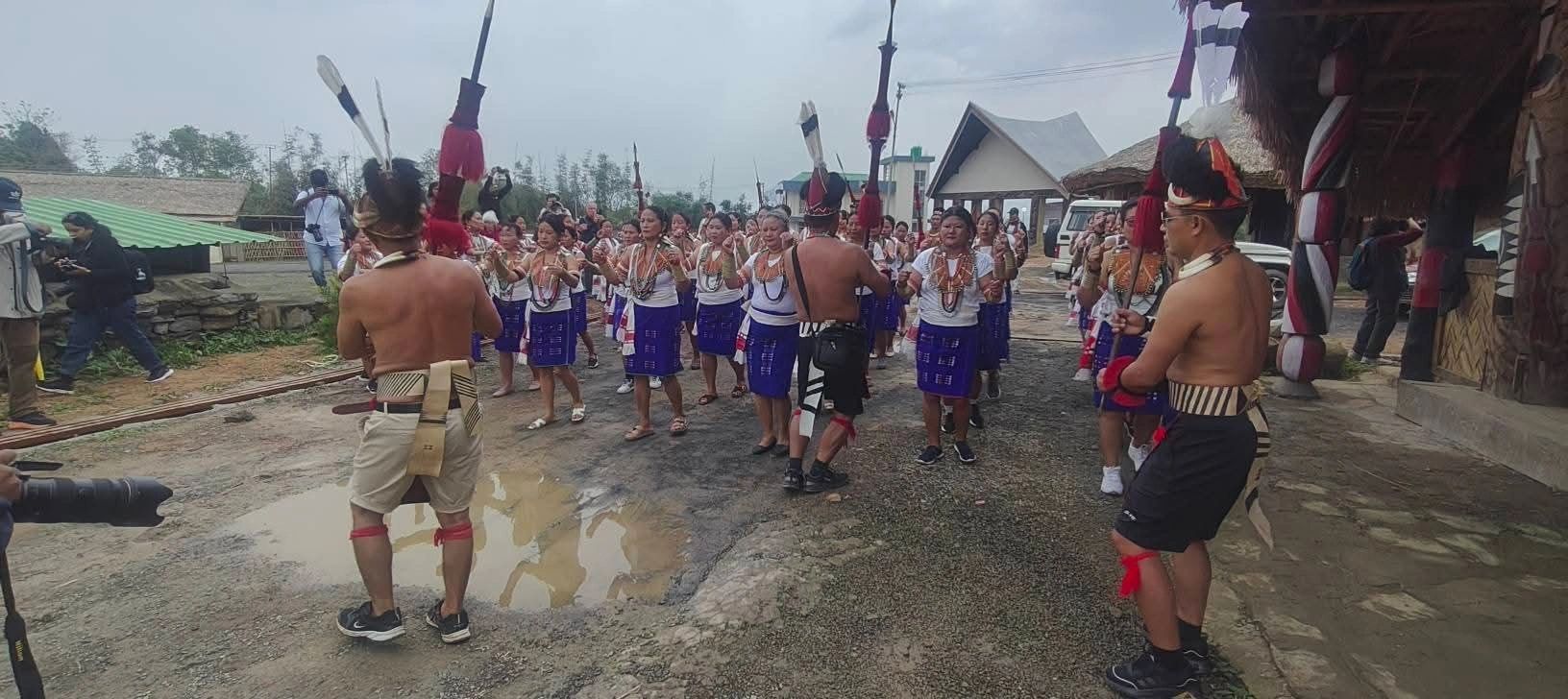 Two lines of Konyak women dancing while warriors in feathered headgear face them during village celebrations at Aoleang in Mon district
