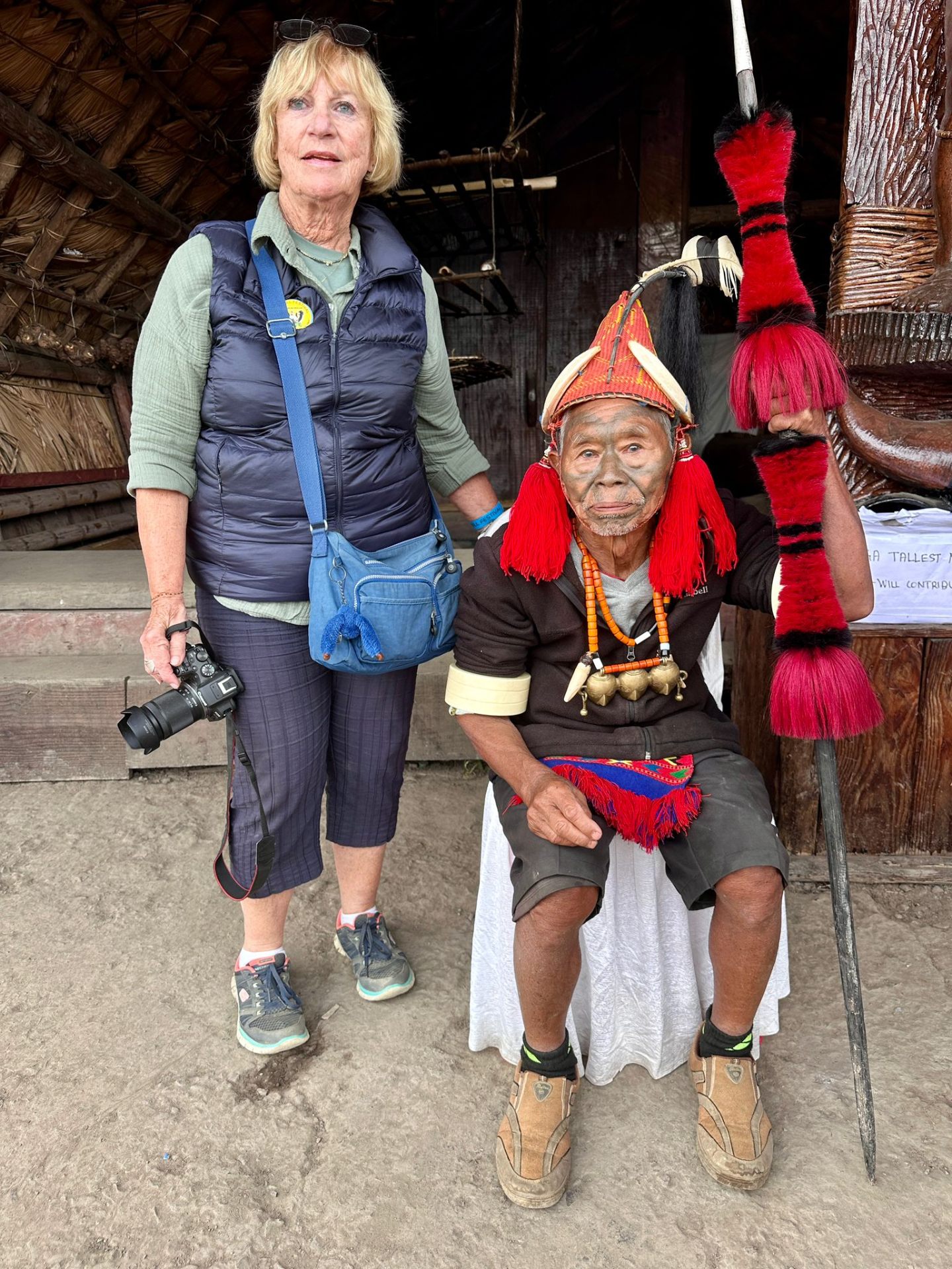 A visiting traveller with a Konyak elder holding a ceremonial staff outside a village morung in Nagaland