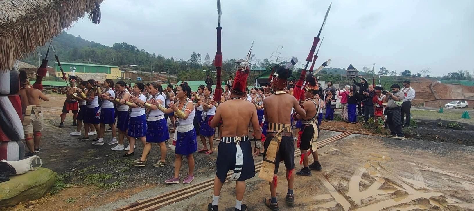 Konyak men with spears and headgear dancing on the open festival ground beside the log drum shed during Aoleang in Mon, Nagaland
