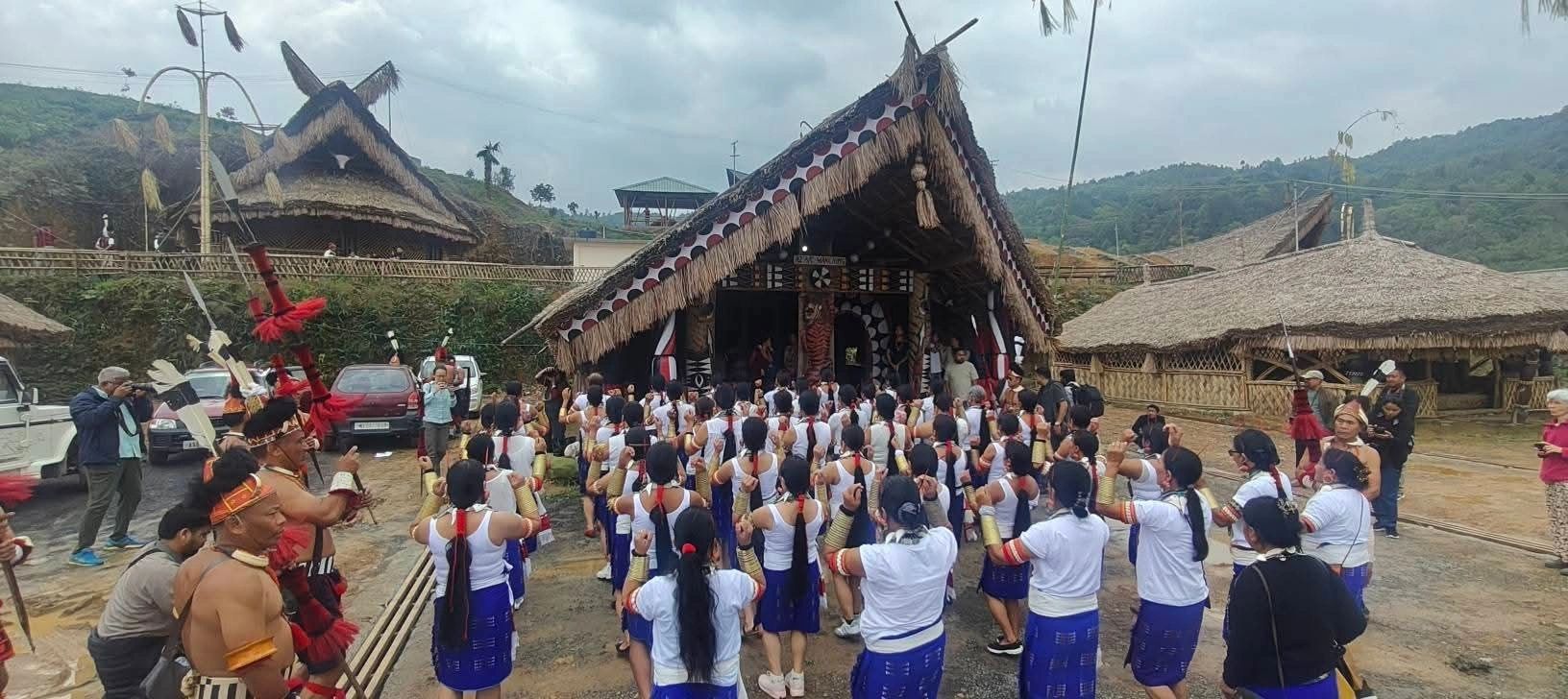 Painted gable and carved facade of a Konyak morung with dancers assembling below during Aoleang Festival, Mon district, Nagaland