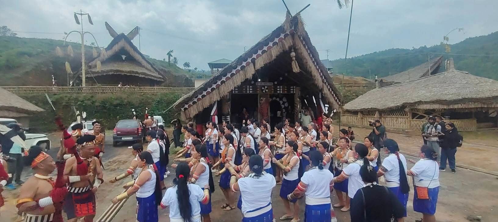 Konyak women in blue wrap-skirts and brass arm rings dancing before a thatched morung during Aoleang Festival in Mon district, Nagaland