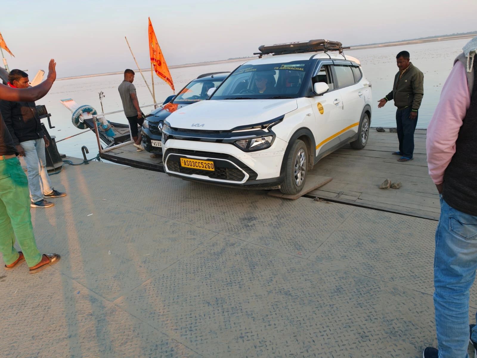 A white SUV being guided onto the wooden deck of a Brahmaputra ferry at a sandy ghat on the way to Majuli, Assam